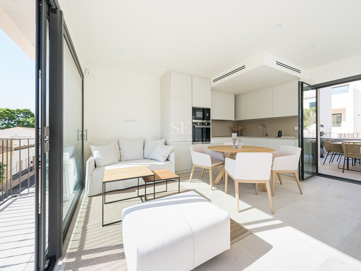 Salón y comedor luminoso de planta abierta con muebles blancos, detalles en madera y grandes ventanales a la terraza.