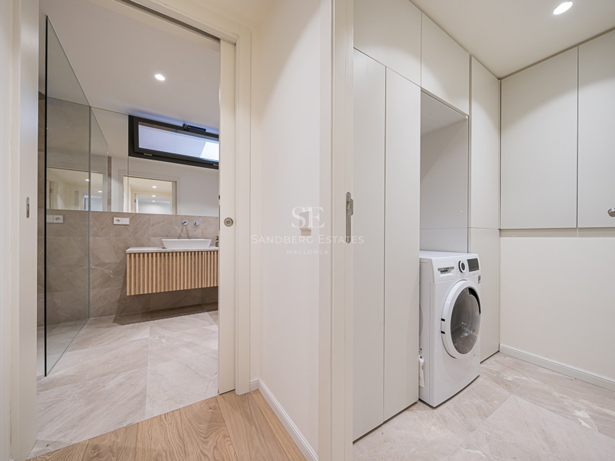 Zona de lavandería moderna con lavadora blanca y armarios empotrados junto a un baño de piedra con lavabo de diseño.