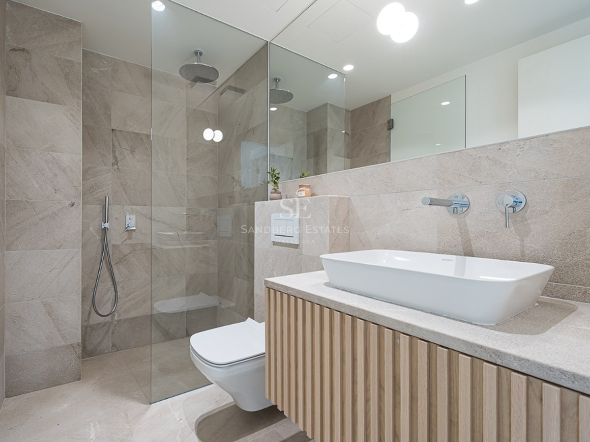 Baño contemporáneo con azulejos de piedra beige, ducha de cristal y mueble de lavabo con listones de madera.