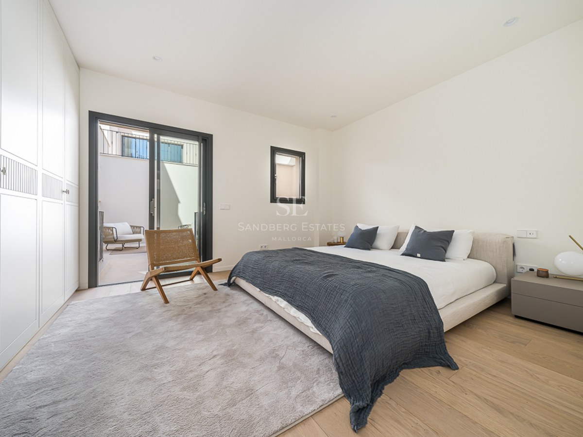 Dormitorio principal con armarios empotrados blancos, suelo de roble y acceso a terraza mediante puerta corredera.