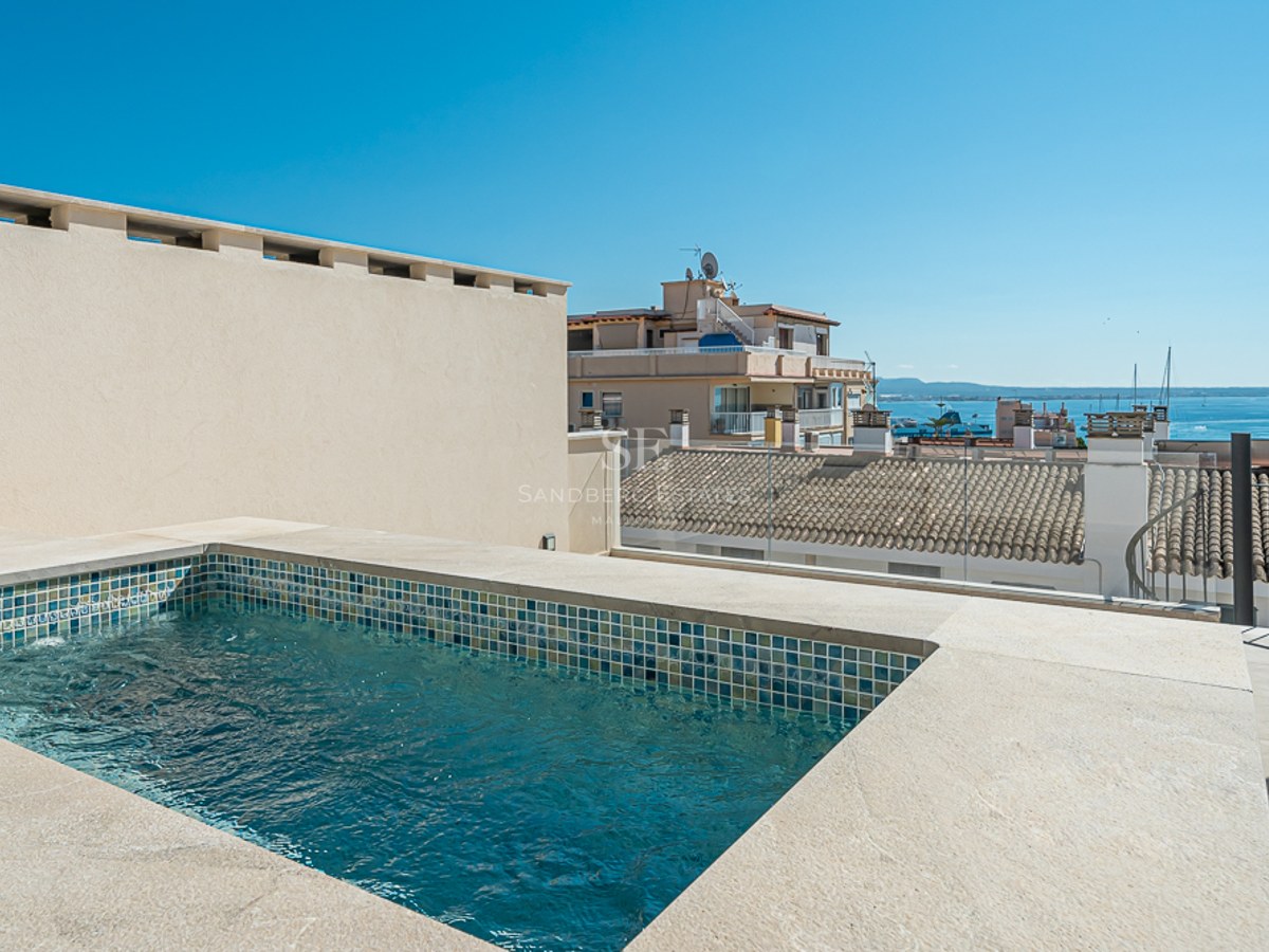 Moderna piscina en azotea rodeada de piedra natural con vistas a los tejados de la ciudad y al mar Mediterráneo.