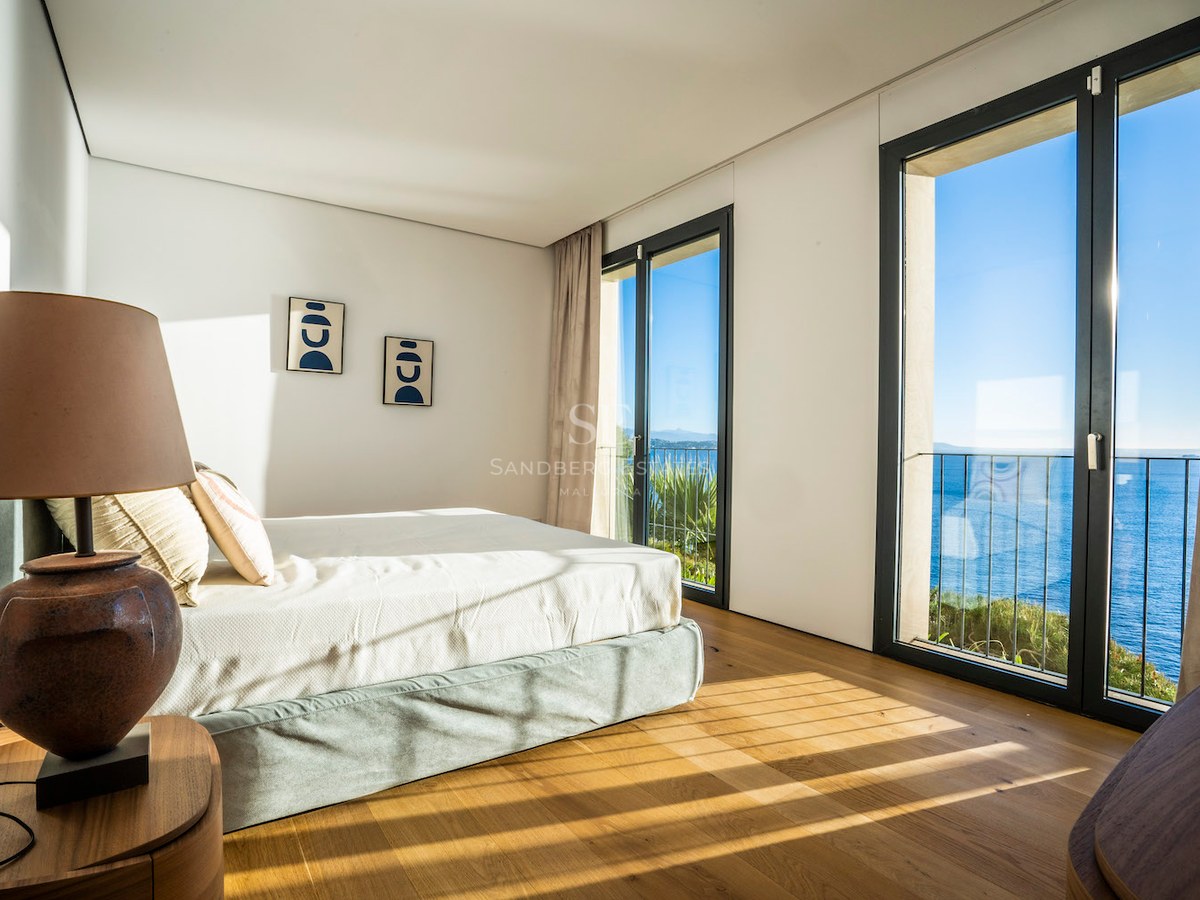 Modern master bedroom featuring oak flooring, floor-to-ceiling windows, and a view of the blue Mediterranean sea.