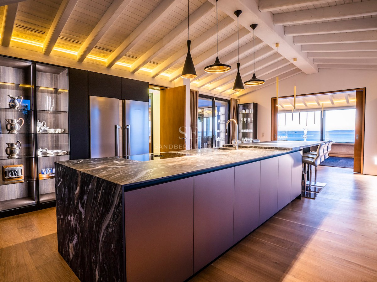 Modern kitchen featuring a large marble island, dark cabinetry, wood beamed ceilings, and a sea view.
