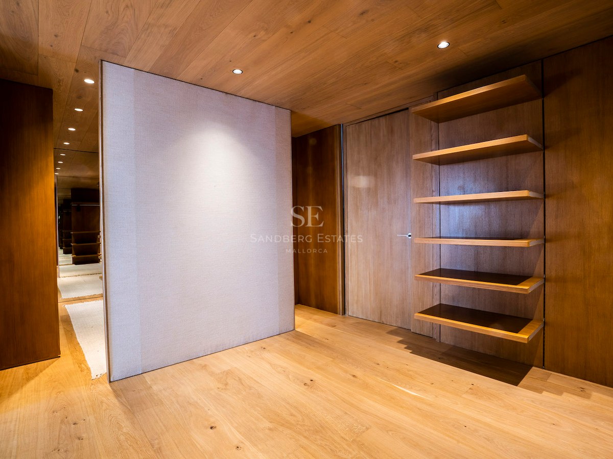 Minimalist dressing room with natural oak wood walls, ceiling, and floor, featuring built-in shelves and warm lighting.