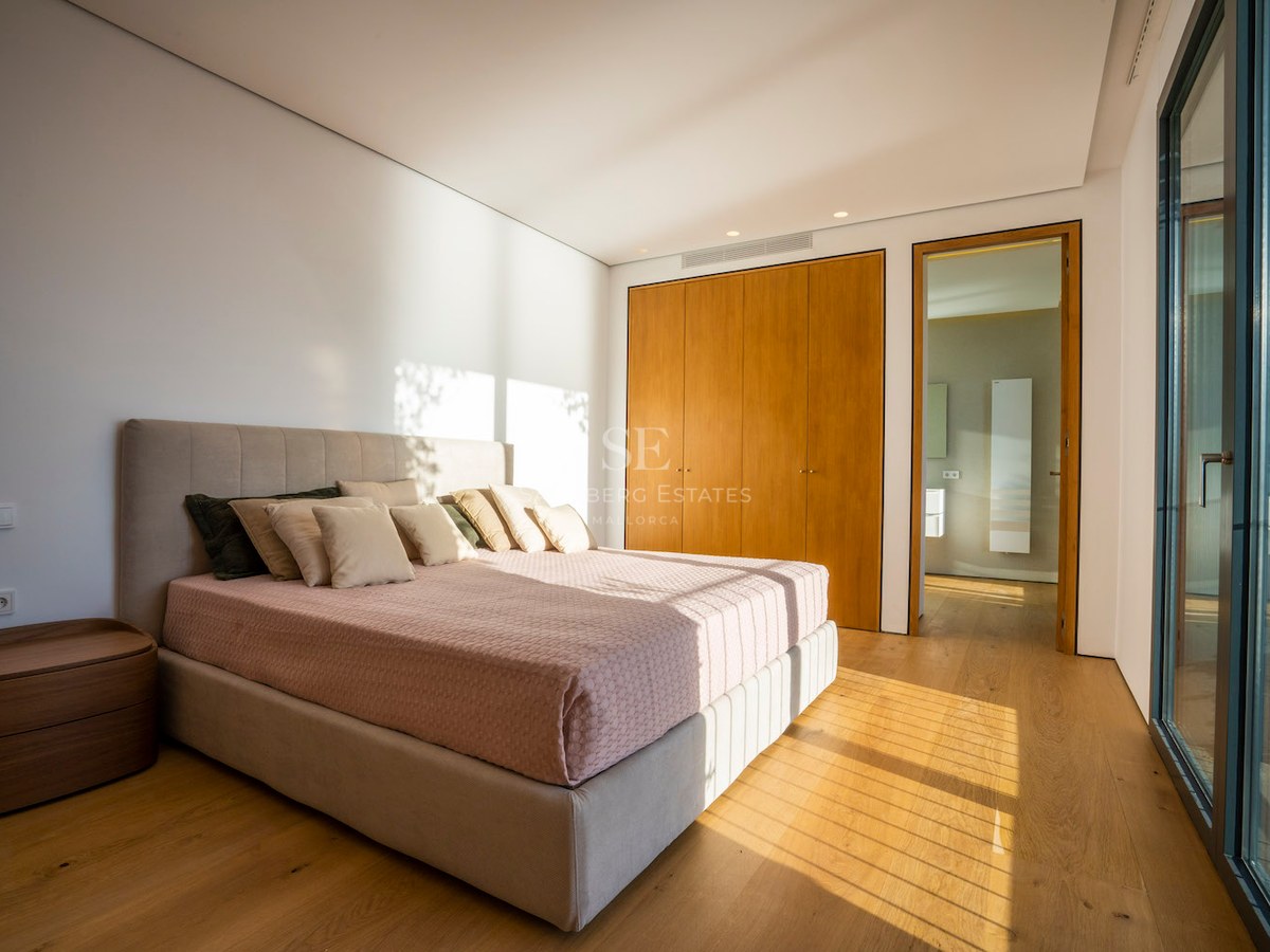 Modern bedroom with oak floors, built-in wooden wardrobes, a large bed, and floor-to-ceiling glass doors.