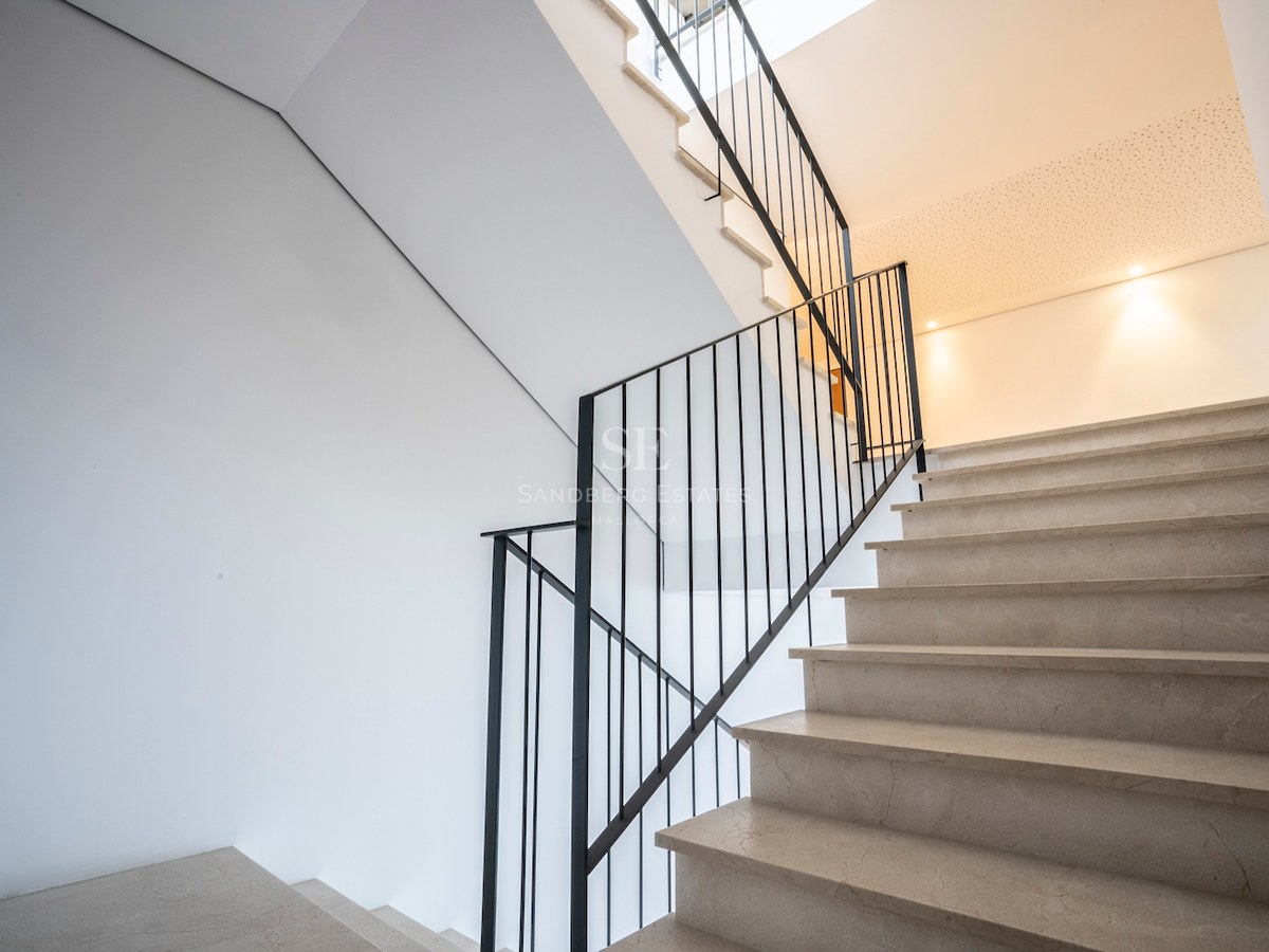 Cream marble staircase with black iron railing against white walls under soft natural light.