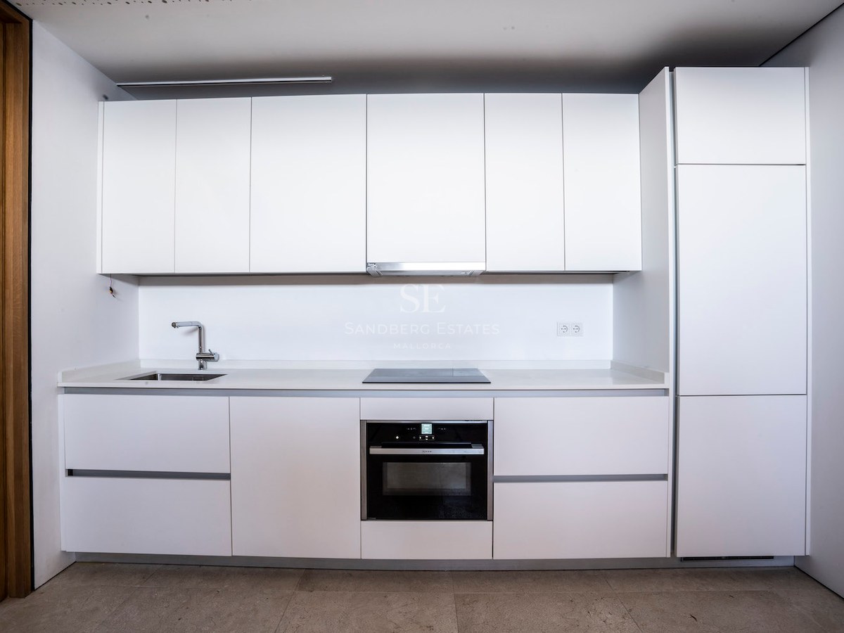 Modern white kitchen with handleless cabinetry, integrated oven, induction hob, and stainless steel sink.