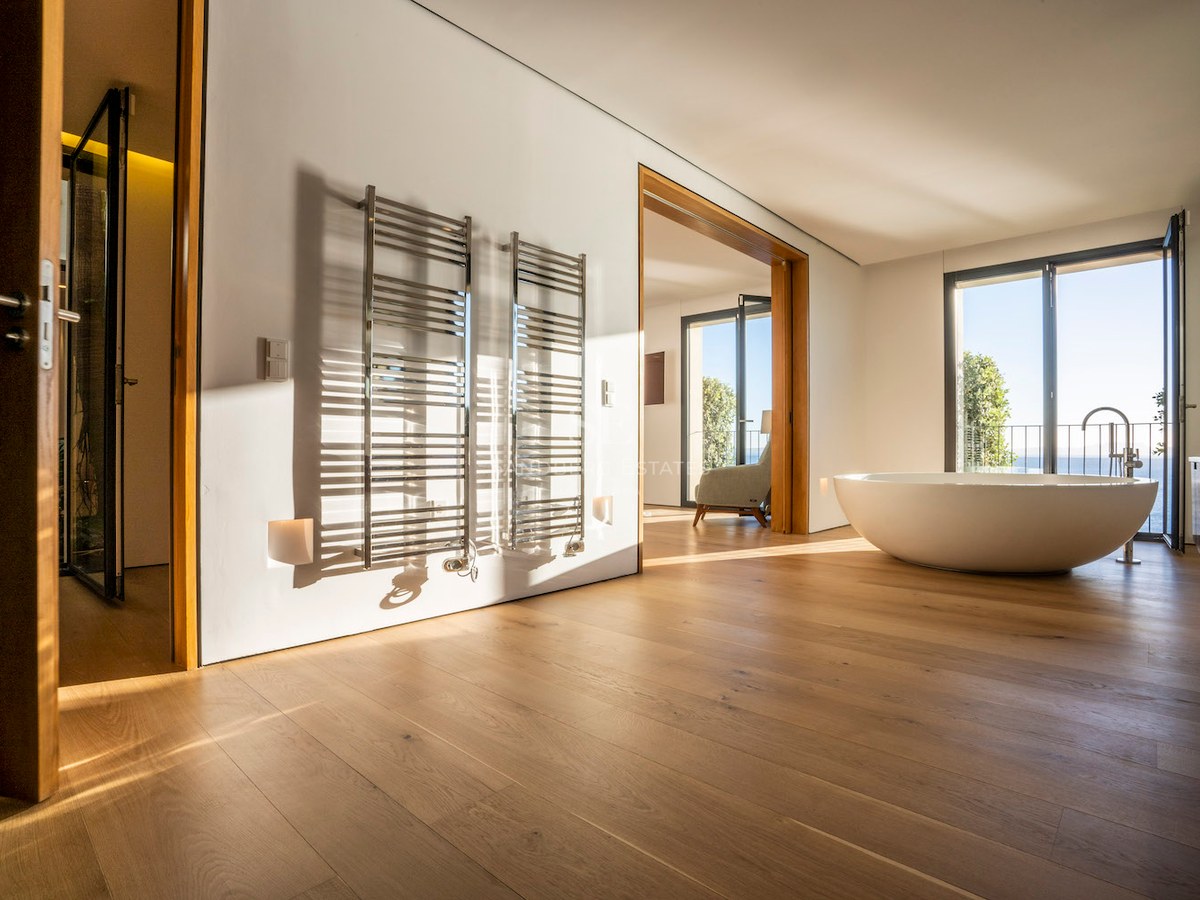 Minimalist master bathroom with oak floors, oval freestanding tub, chrome towel rails, and Mediterranean sea views.