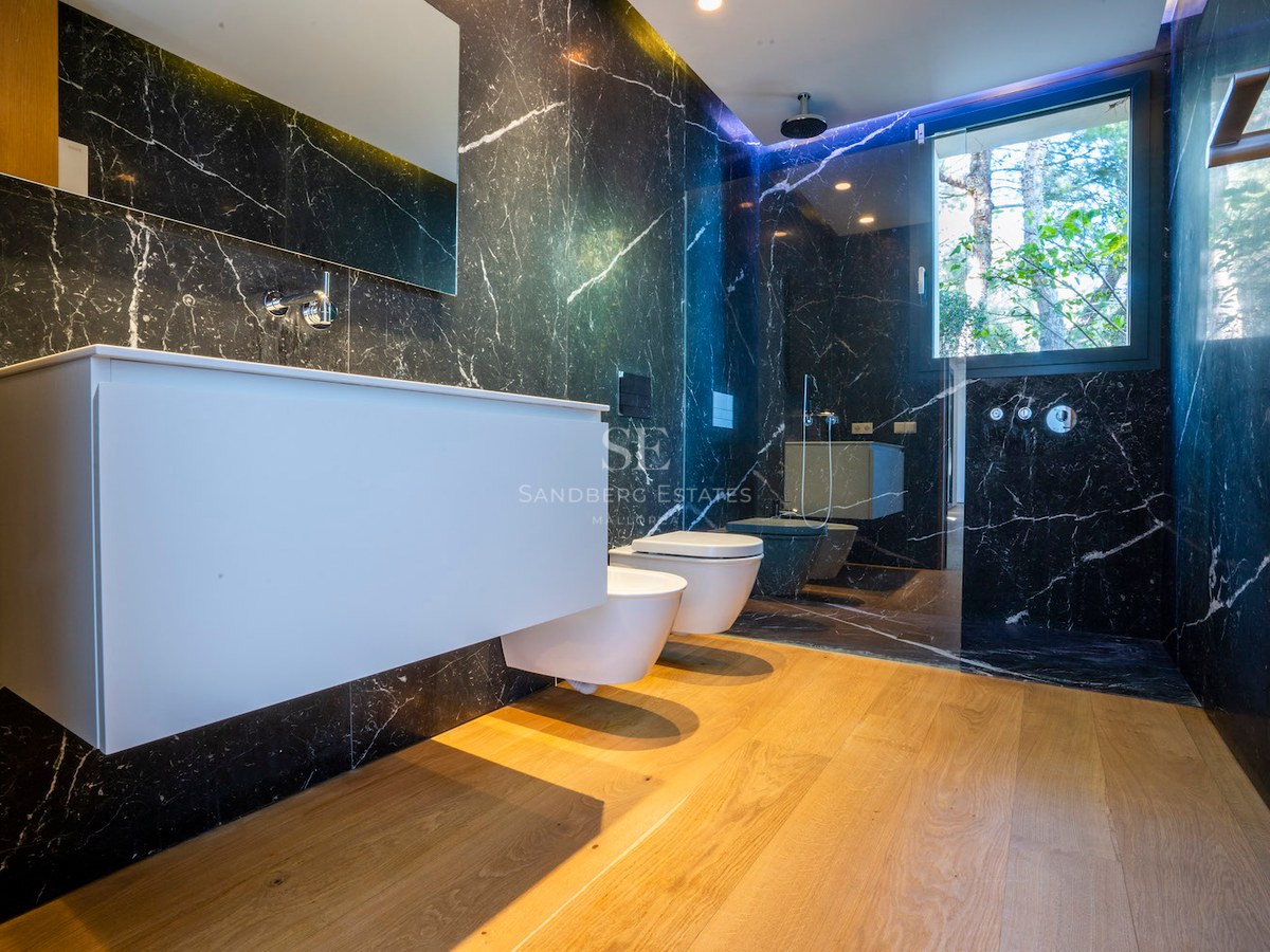 Modern bathroom with black veined marble walls, oak flooring, floating white vanity, and walk-in glass shower.