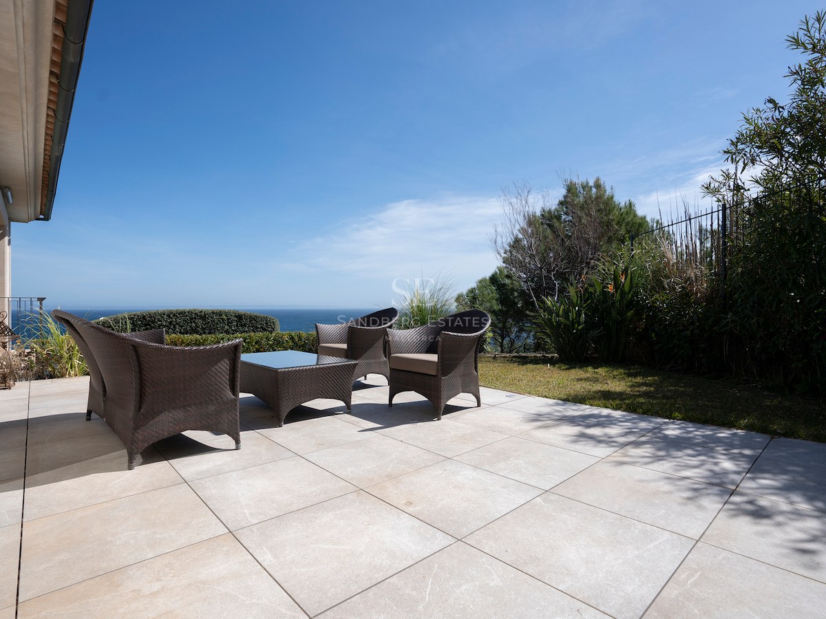 Large stone tile terrace with dark wicker lounge furniture overlooking the ocean under a clear blue sky.