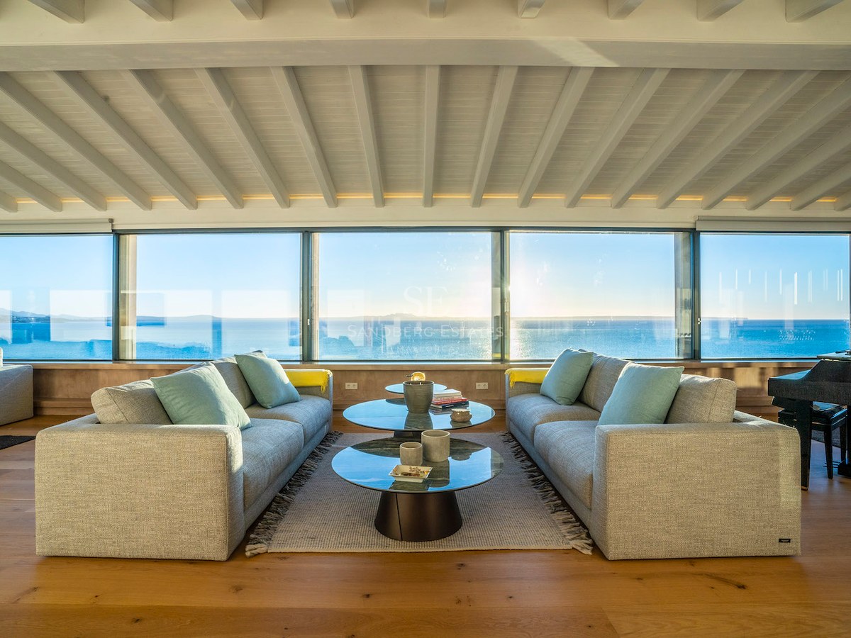 Modern living room featuring grey sofas, glass coffee tables, and floor-to-ceiling windows overlooking the Mediterranean.