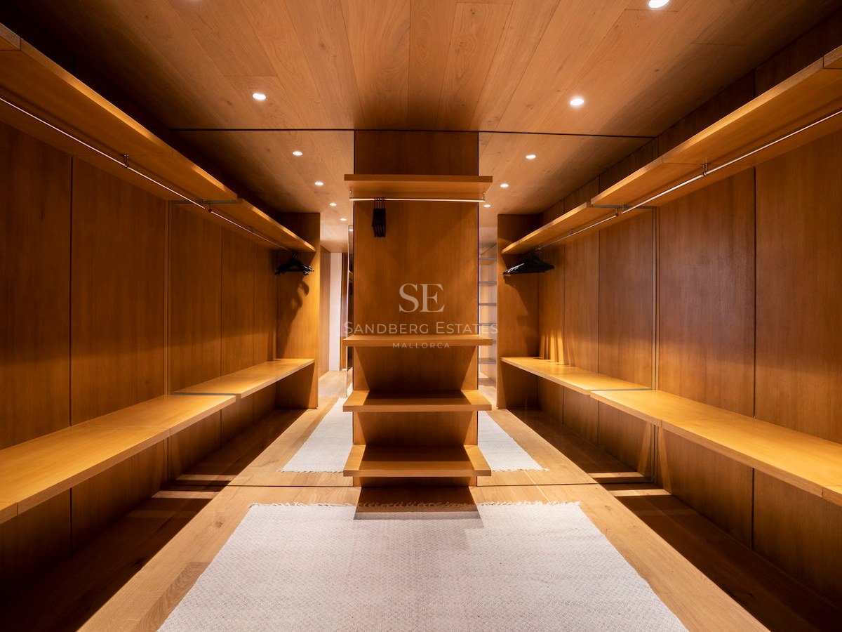 Symmetrical walk-in closet with floor-to-ceiling oak wood paneling, open shelving, and integrated warm lighting.