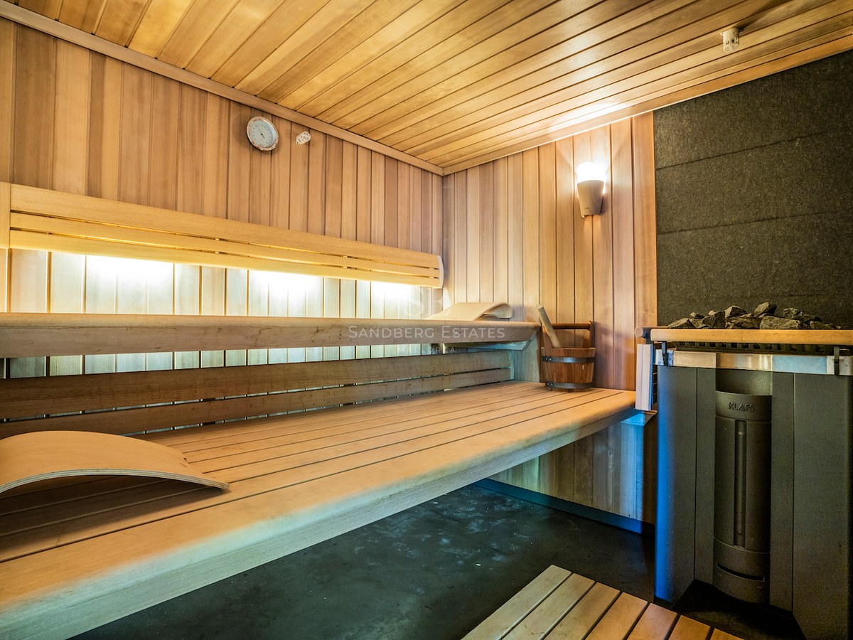 Interior of a modern wooden sauna with multi-level benches, ambient lighting, and a professional KLAFS heater.