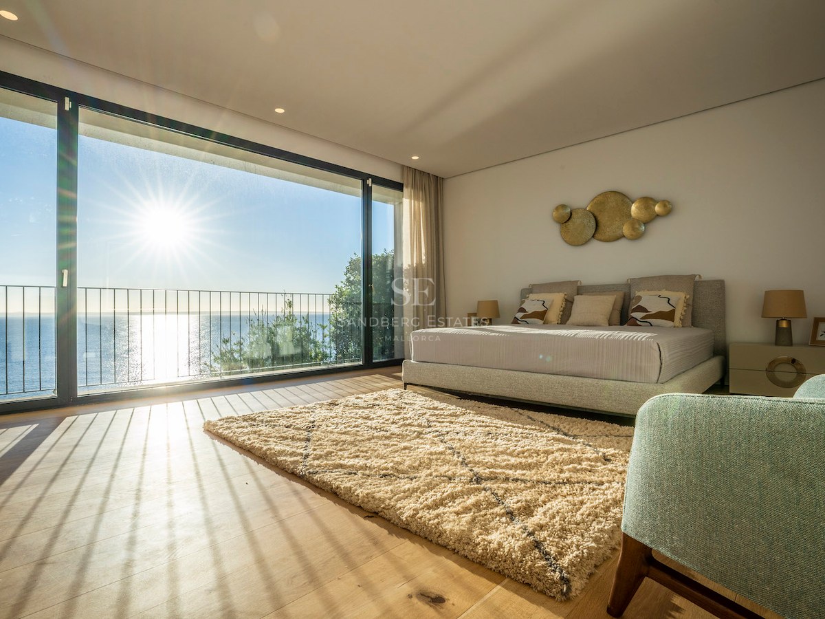 Bright master bedroom featuring floor-to-ceiling glass doors, oak flooring, and a terrace overlooking the blue sea.