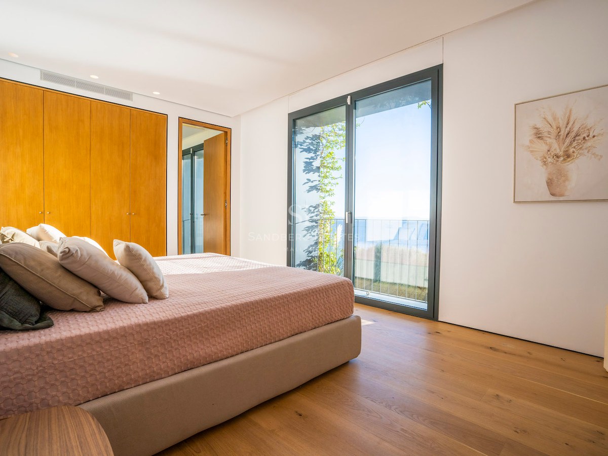 Bedroom featuring oak flooring, built-in wooden wardrobes, and floor-to-ceiling glass doors overlooking the sea.