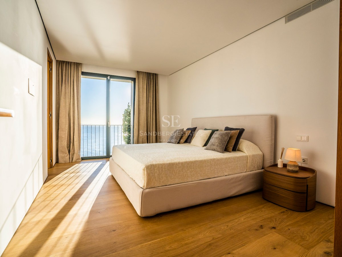 Modern bedroom featuring oak floors and floor-to-ceiling glass doors opening to a Mediterranean sea view.
