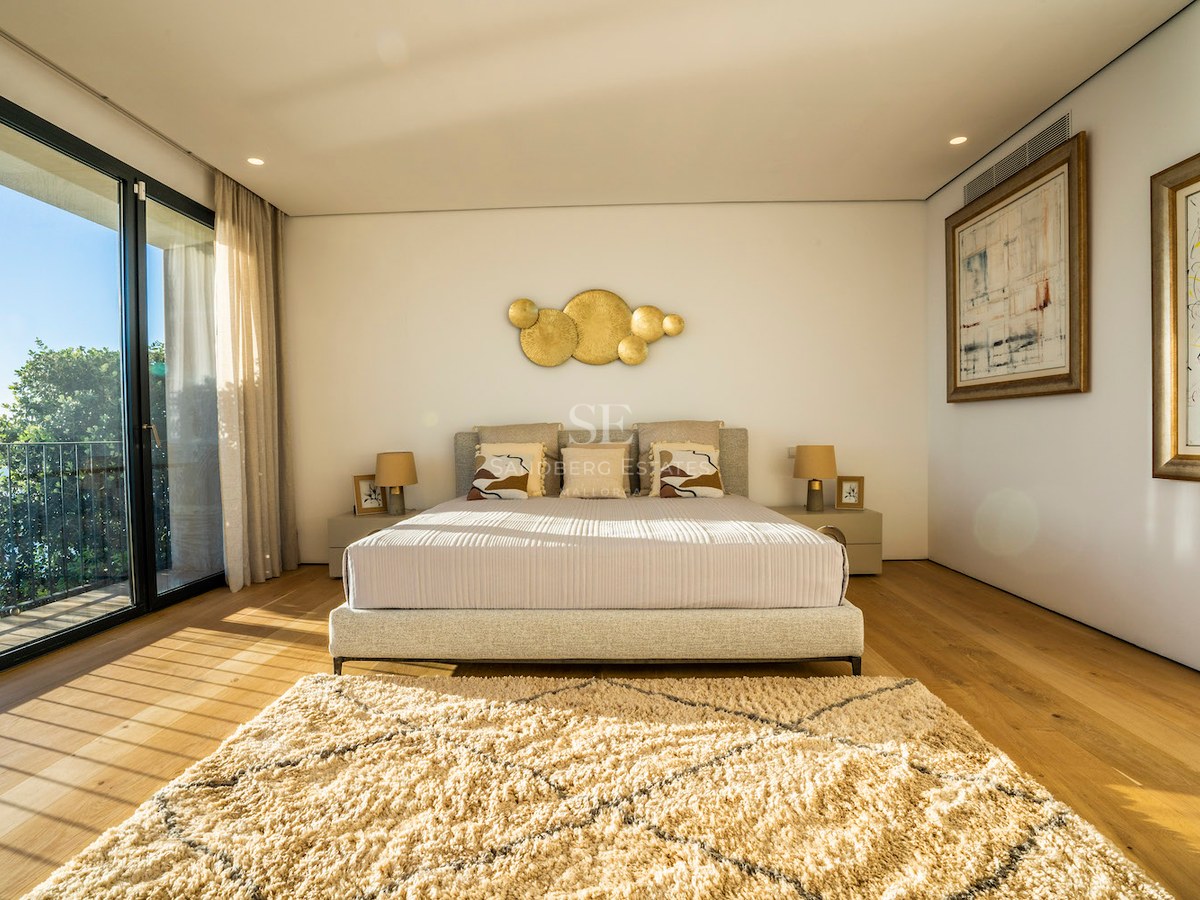 Modern master bedroom with oak floors, floor-to-ceiling glass doors opening to a terrace with sea views and natural light.