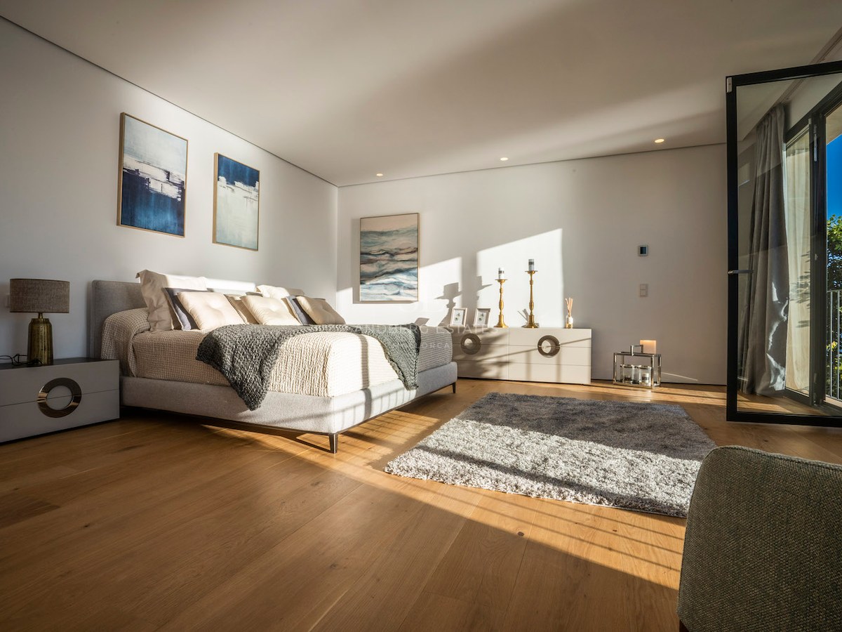 Modern master bedroom featuring a king-size bed, light oak floors, floor-to-ceiling glass door, and direct sunlight.