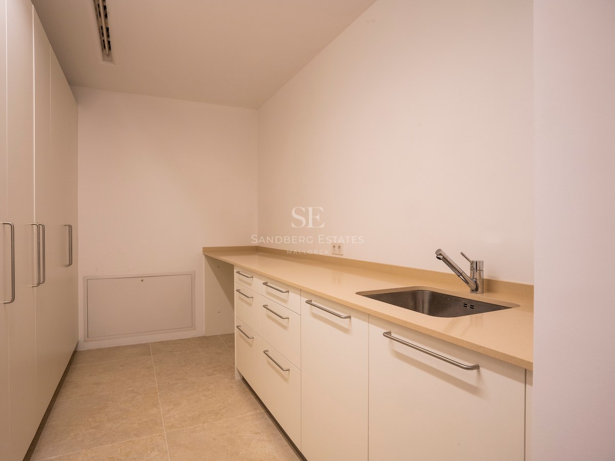 White utility room featuring a long beige countertop, stainless steel sink, and floor-to-ceiling storage cabinets.