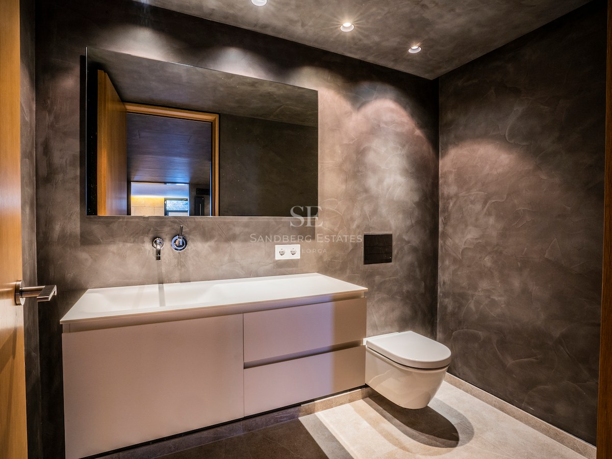 Contemporary bathroom featuring charcoal microcement walls, a white wall-hung vanity, and a large frameless mirror.