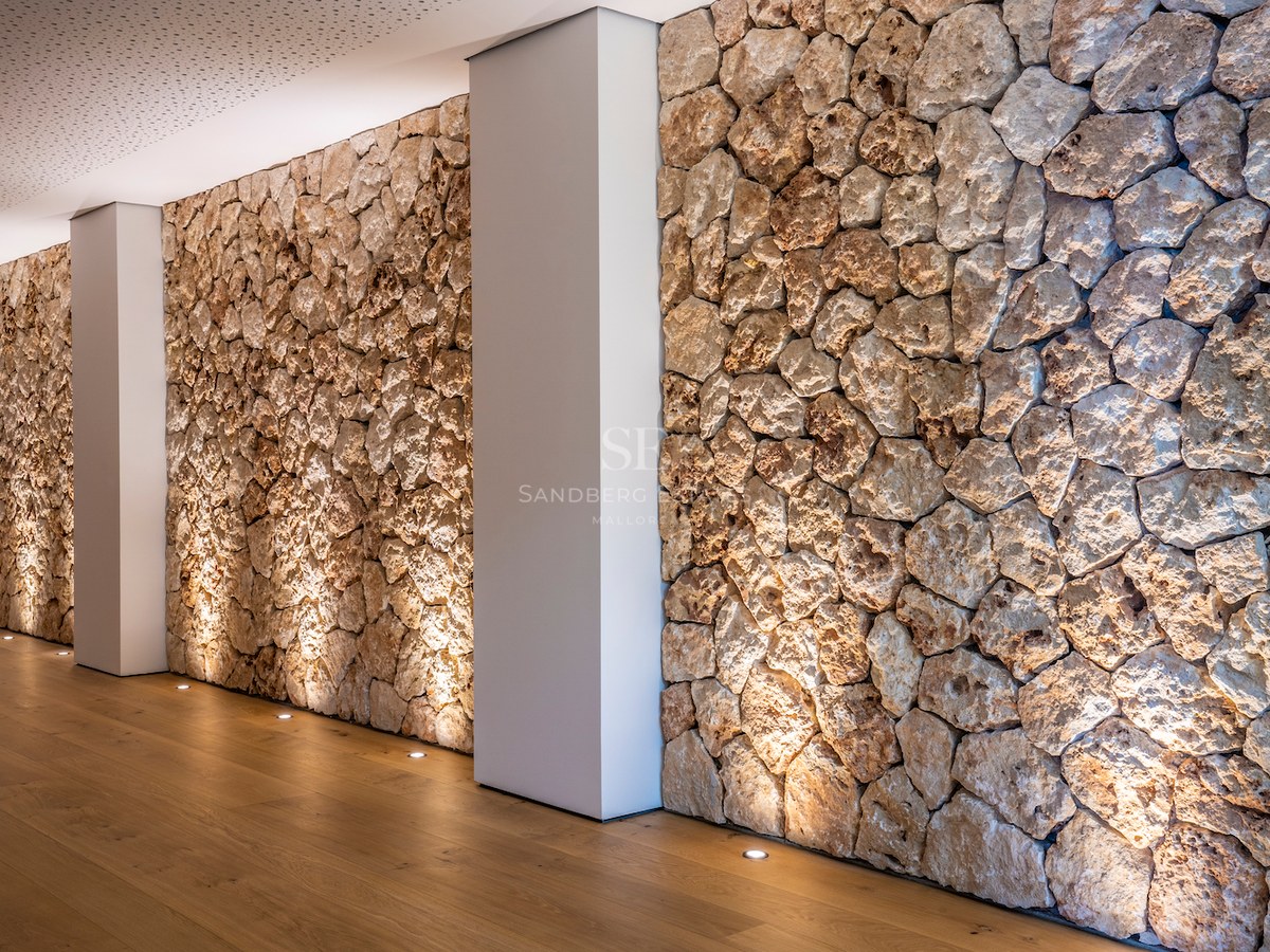 Interior corridor featuring a rustic dry-stone wall illuminated by floor uplights and light oak flooring.