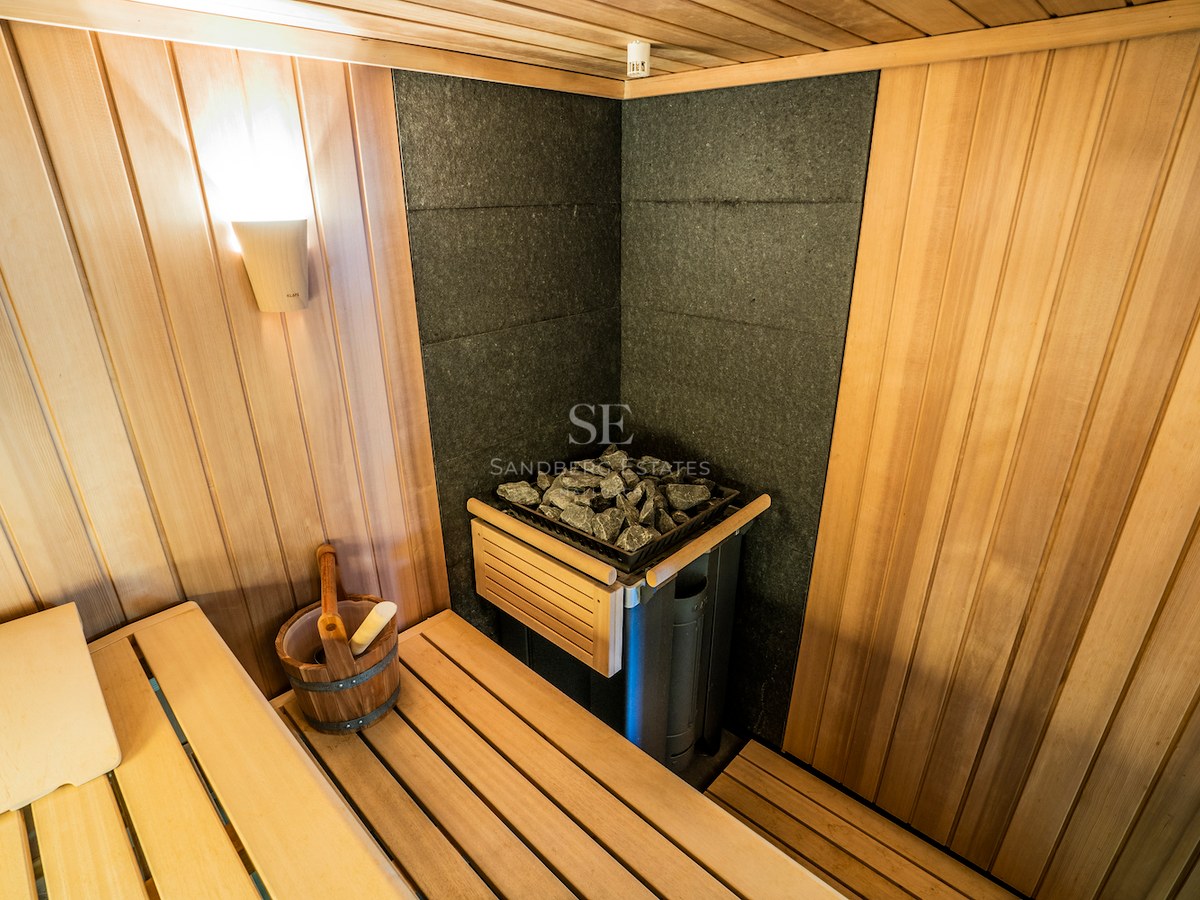 Interior of a wood-paneled sauna featuring a KLAFS stone heater, wooden bucket, and atmospheric lighting.