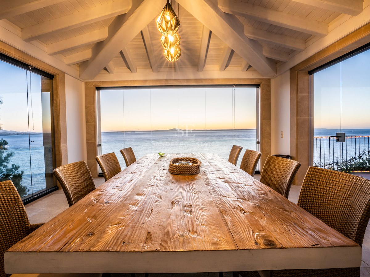 Large wooden dining table on a glass-enclosed terrace with sunset views over the Mediterranean sea.