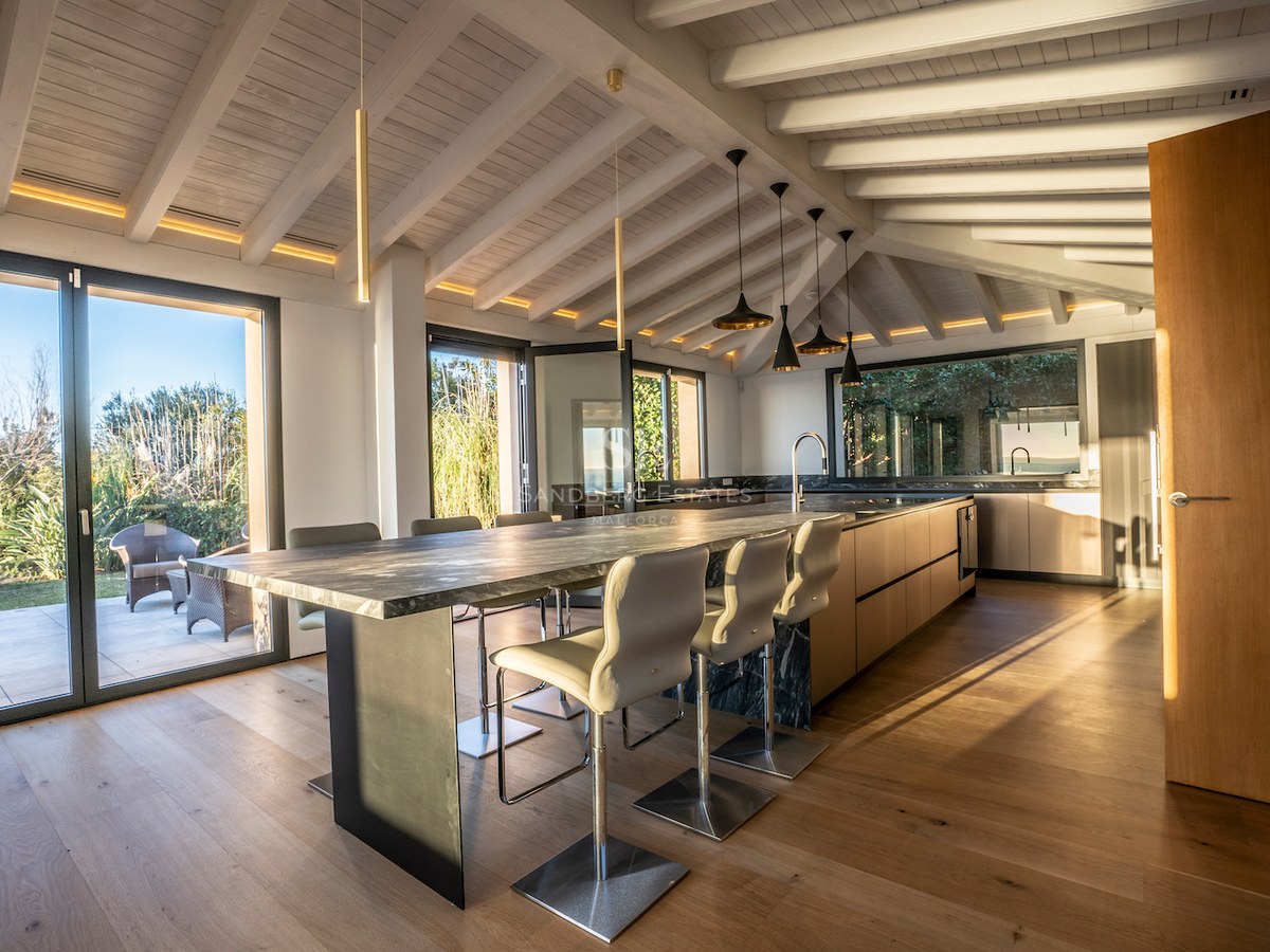 Contemporary kitchen featuring a dark marble island, white wooden beams, and floor-to-ceiling windows to the garden.