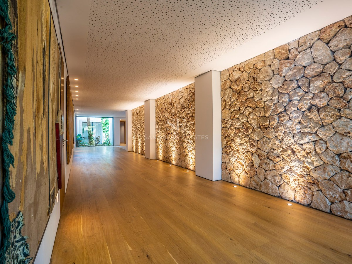 Modern interior hallway featuring a textured stone wall, recessed floor lighting, and light oak wood flooring.