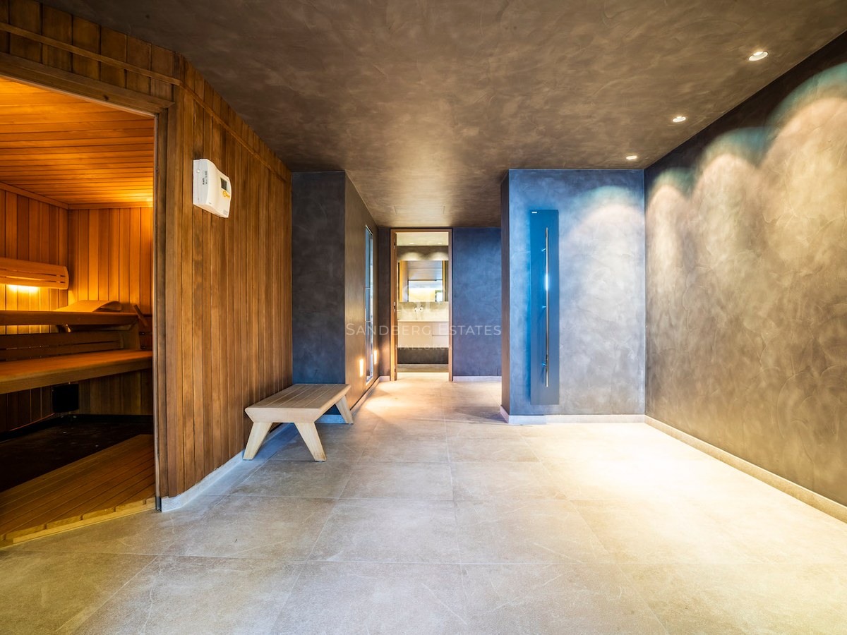 Modern indoor spa area with a wood-lined sauna, grey microcement walls, and large floor tiles under recessed lighting.