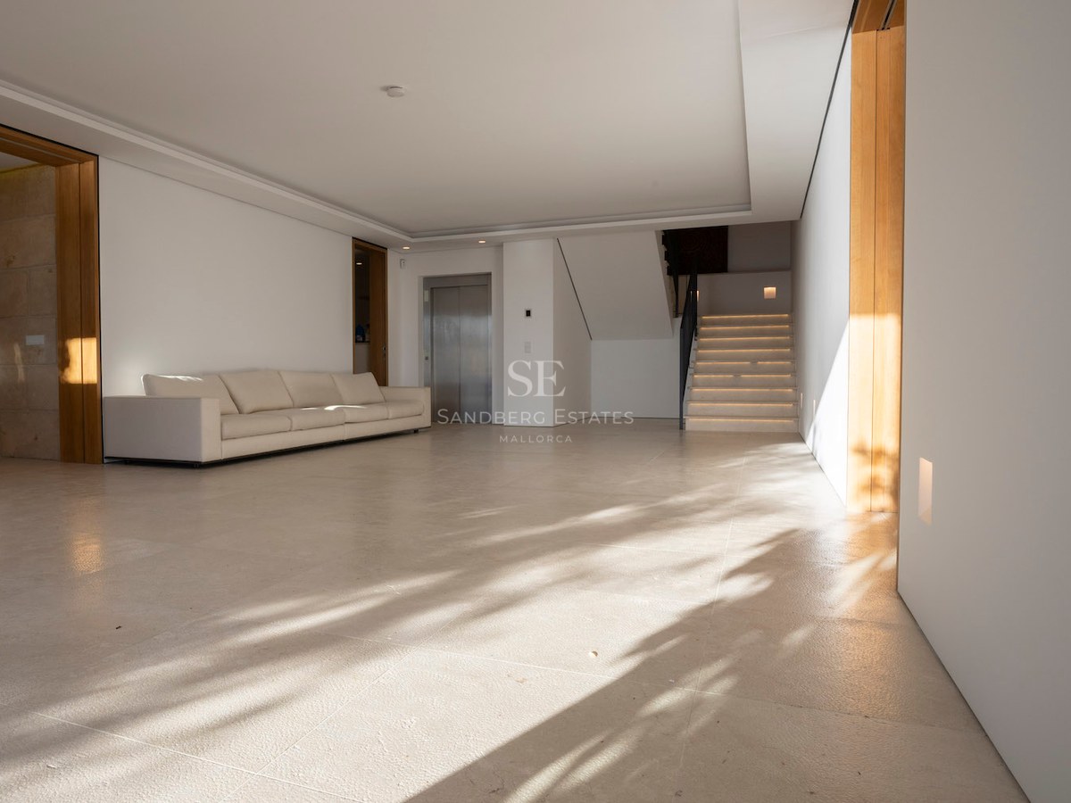 Spacious minimalist hall with cream stone floors, a white sofa, a private elevator, and a stone staircase.