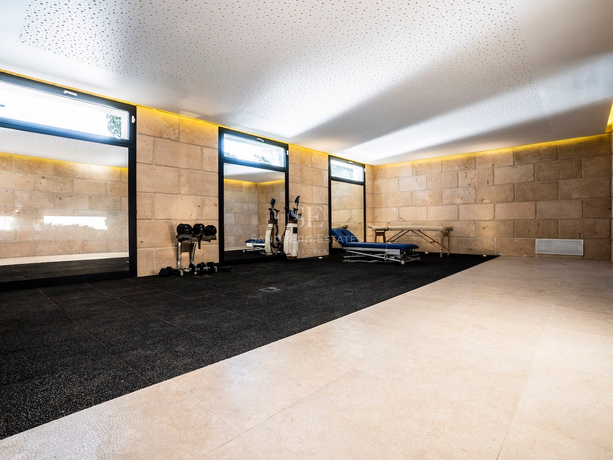 Modern home gym featuring natural stone walls, professional rubber flooring, a massage table, and indirect ceiling lighting.
