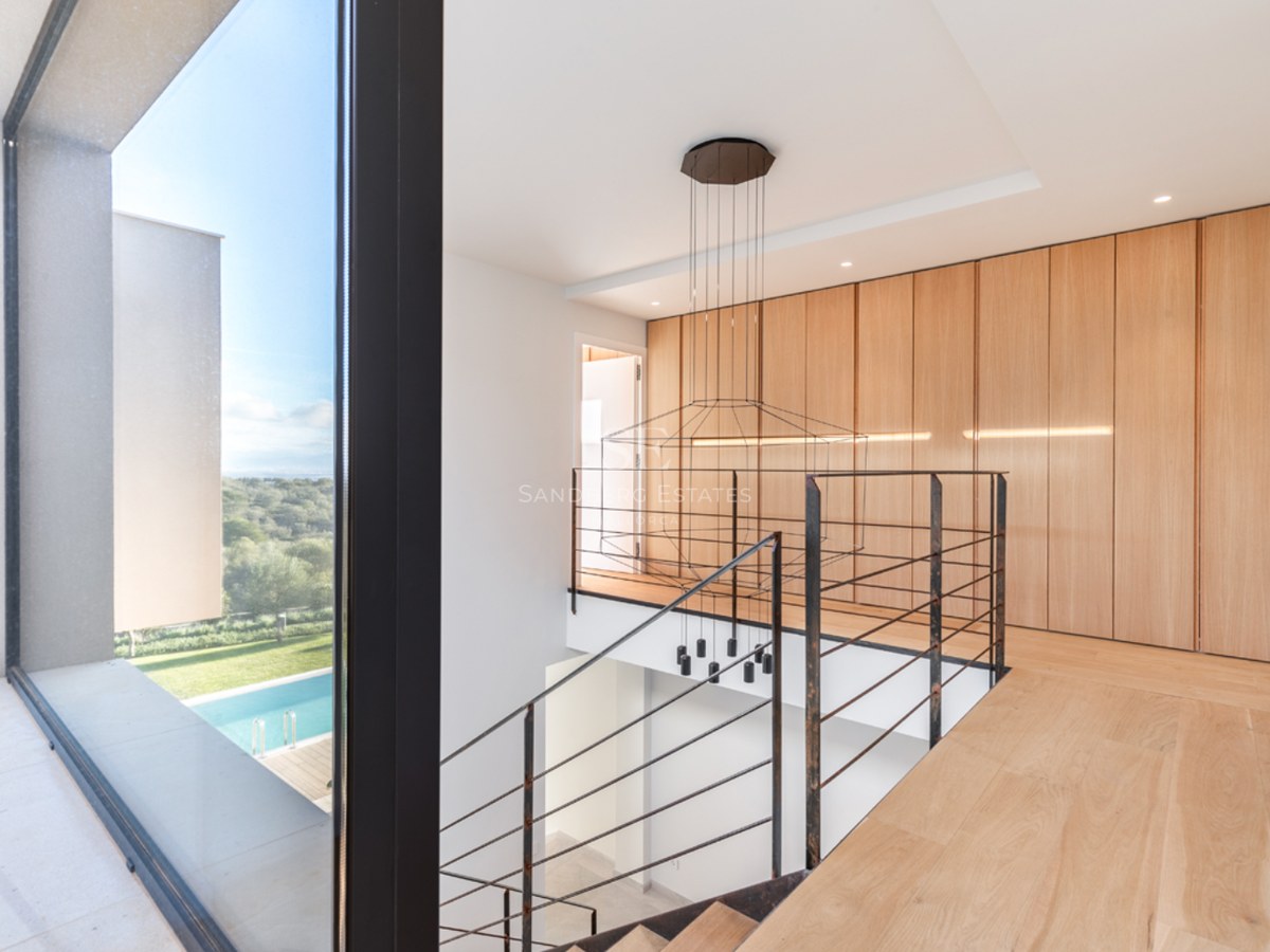Palier moderne à l'étage avec parquet en chêne clair, garde-corps en métal noir et grande baie vitrée vue sur piscine.