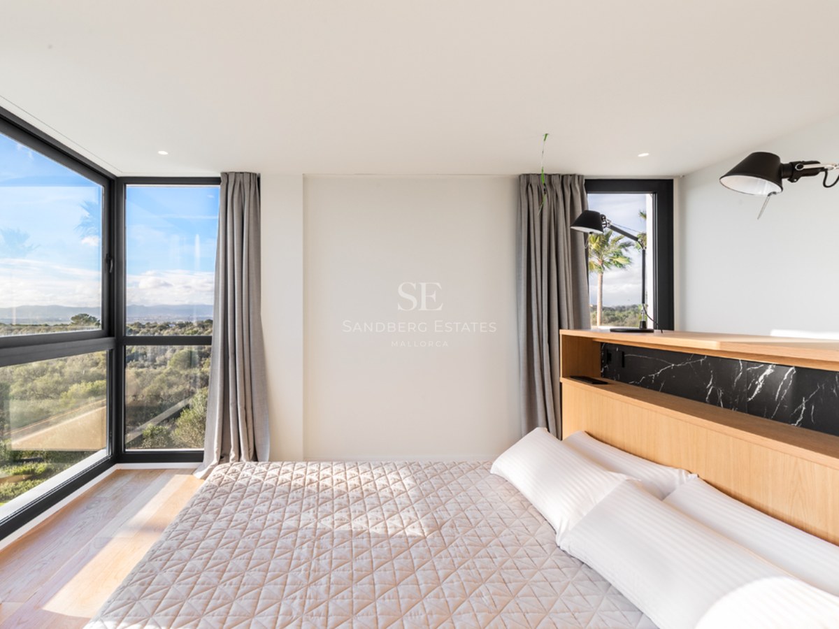 Chambre lumineuse avec tête de lit en chêne, accents de marbre noir et grandes fenêtres d'angle donnant sur la nature.
