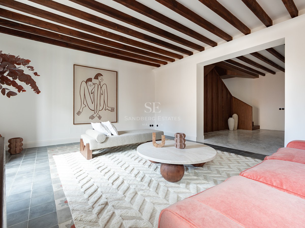 Salón moderno con vigas de madera oscura, sofá de terciopelo terracota, mesa de mármol y suelo de baldosa artesanal.