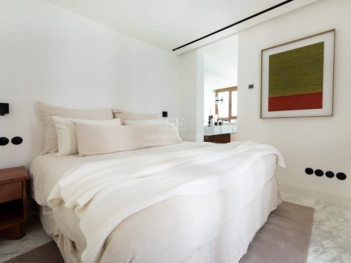 Dormitorio principal contemporáneo con cama grande, suelos de mármol y vista al baño privado con acabados en madera.