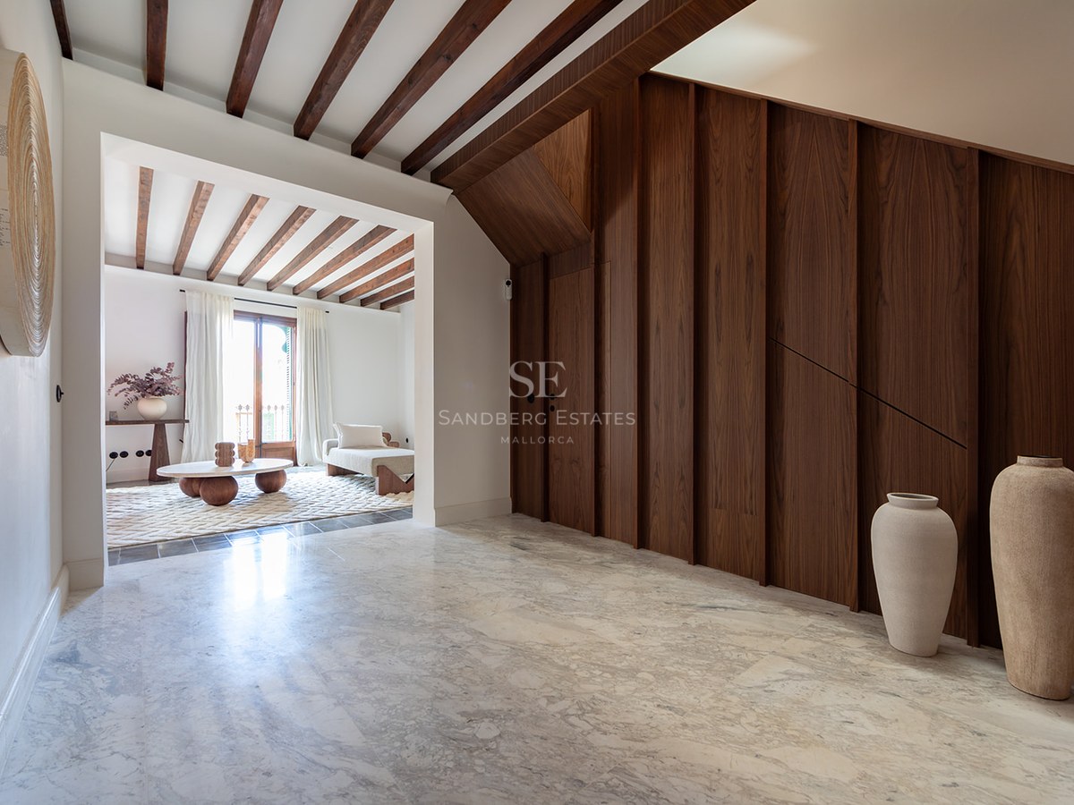 Vestíbulo de lujo con suelo de mármol, panelado de madera oscura y vigas de madera que conecta con el salón.