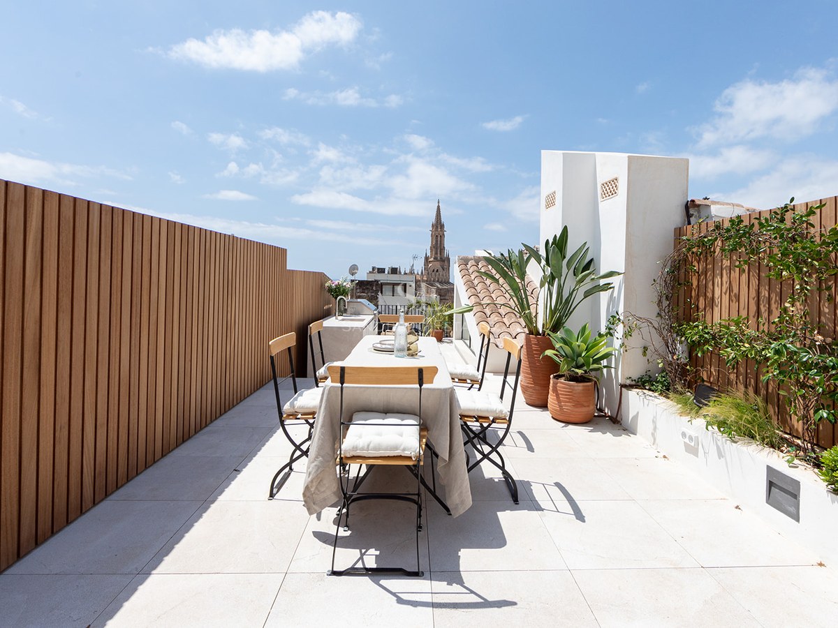 Terraza moderna con mesa de comedor, cercado de madera y vistas a la Catedral de Palma bajo un cielo azul despejado.