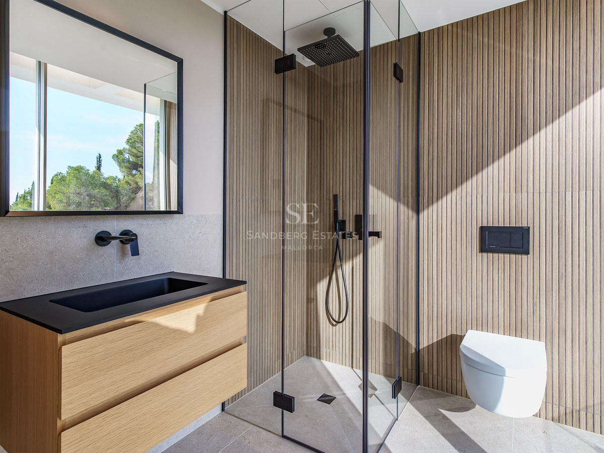 Salle de bain moderne avec murs en lattes de bois, douche en verre, vasque noire et lumière naturelle.