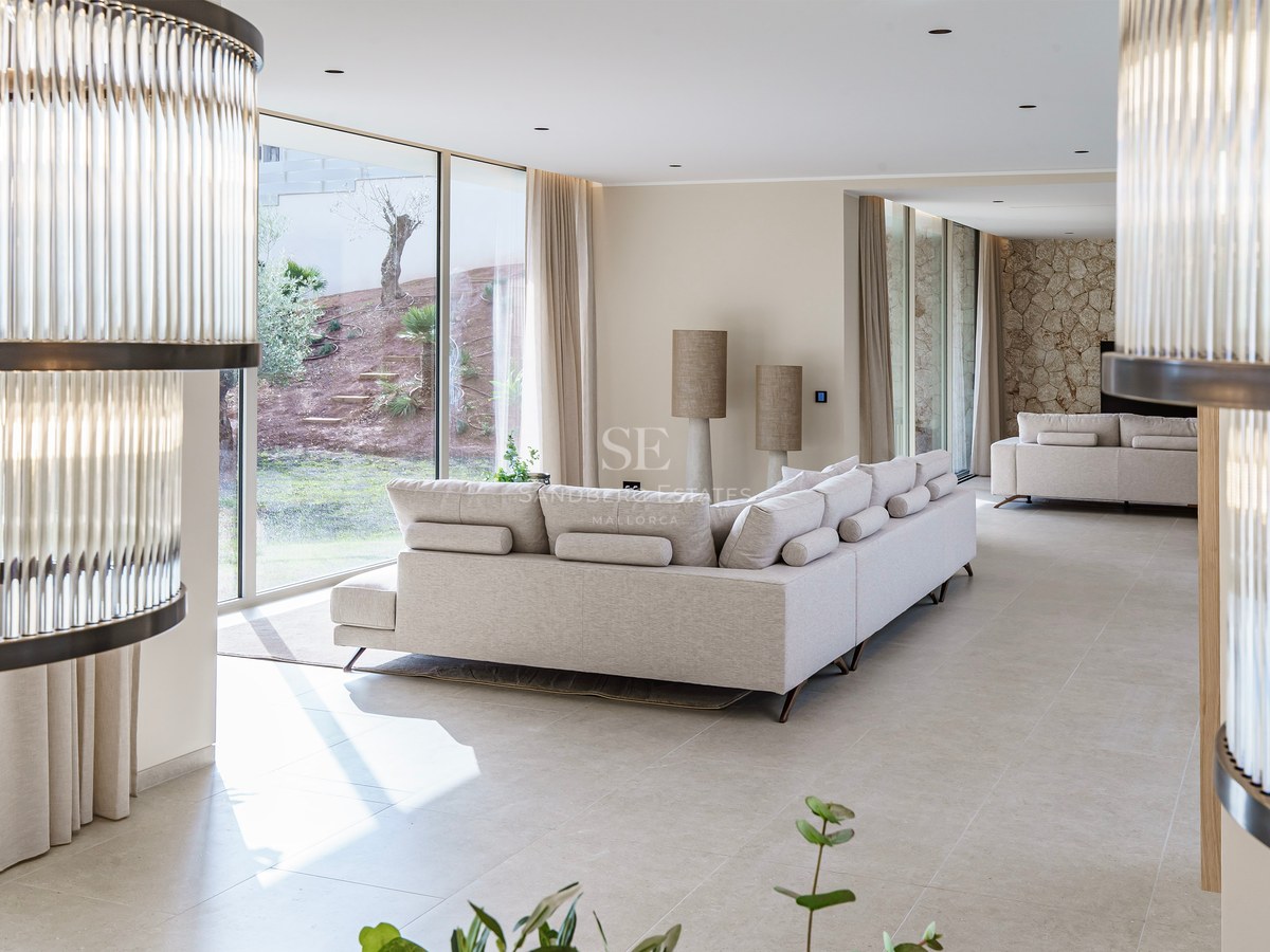 Grand salon moderne avec canapé crème, larges baies vitrées sur le jardin et mur d'accent en pierre.