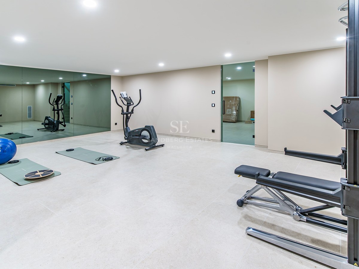Salle de sport avec vélo elliptique, banc de musculation et grands miroirs sous des plafonniers brillants.