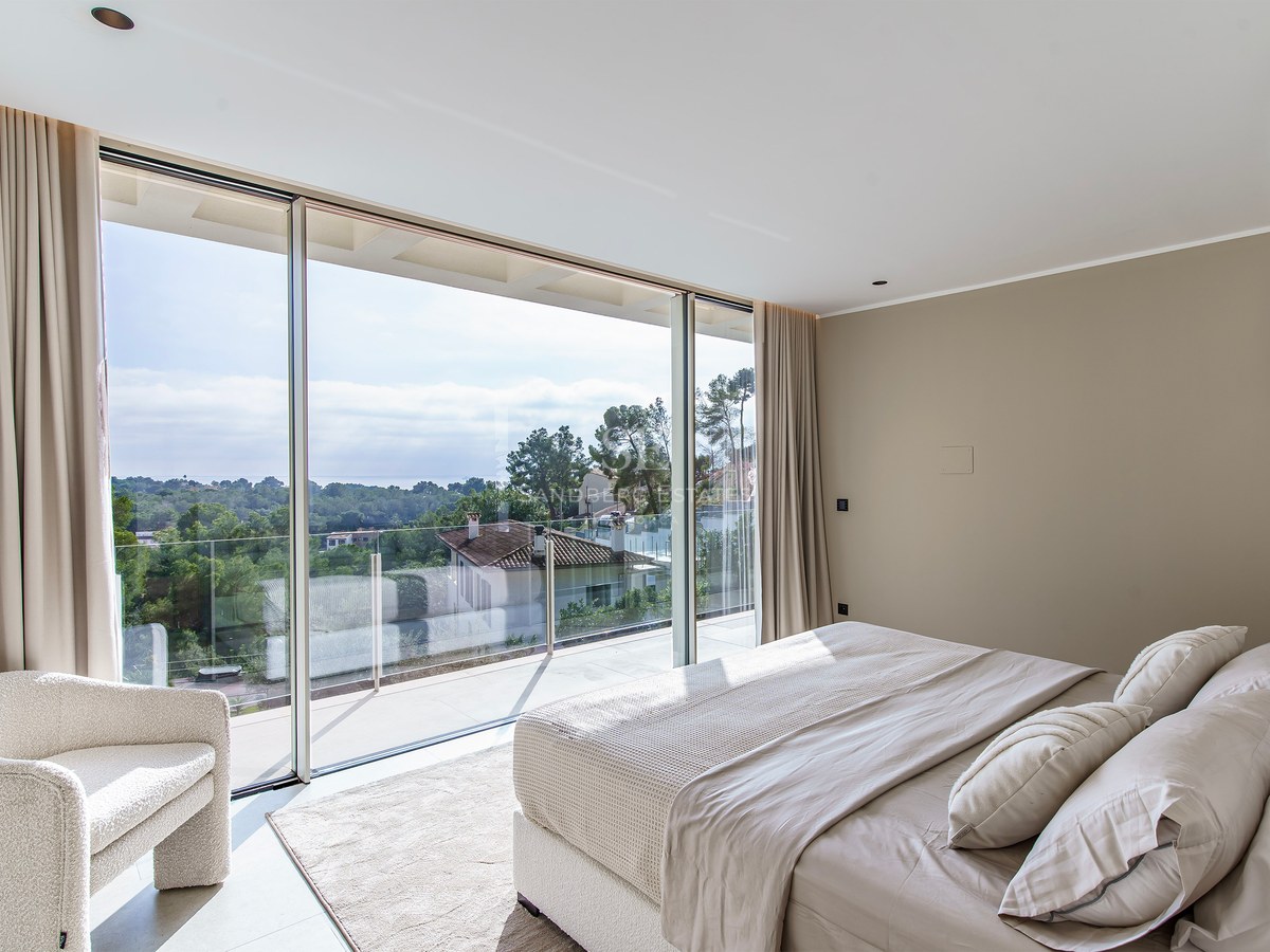 Chambre de luxe avec baies vitrées donnant sur la nature, lit douillet et fauteuil en bouclé.