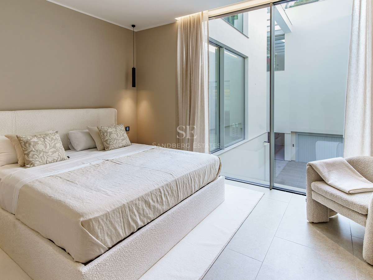 Chambre minimaliste avec lit en bouclé crème, fauteuil assorti et grandes baies vitrées donnant sur un patio intérieur.