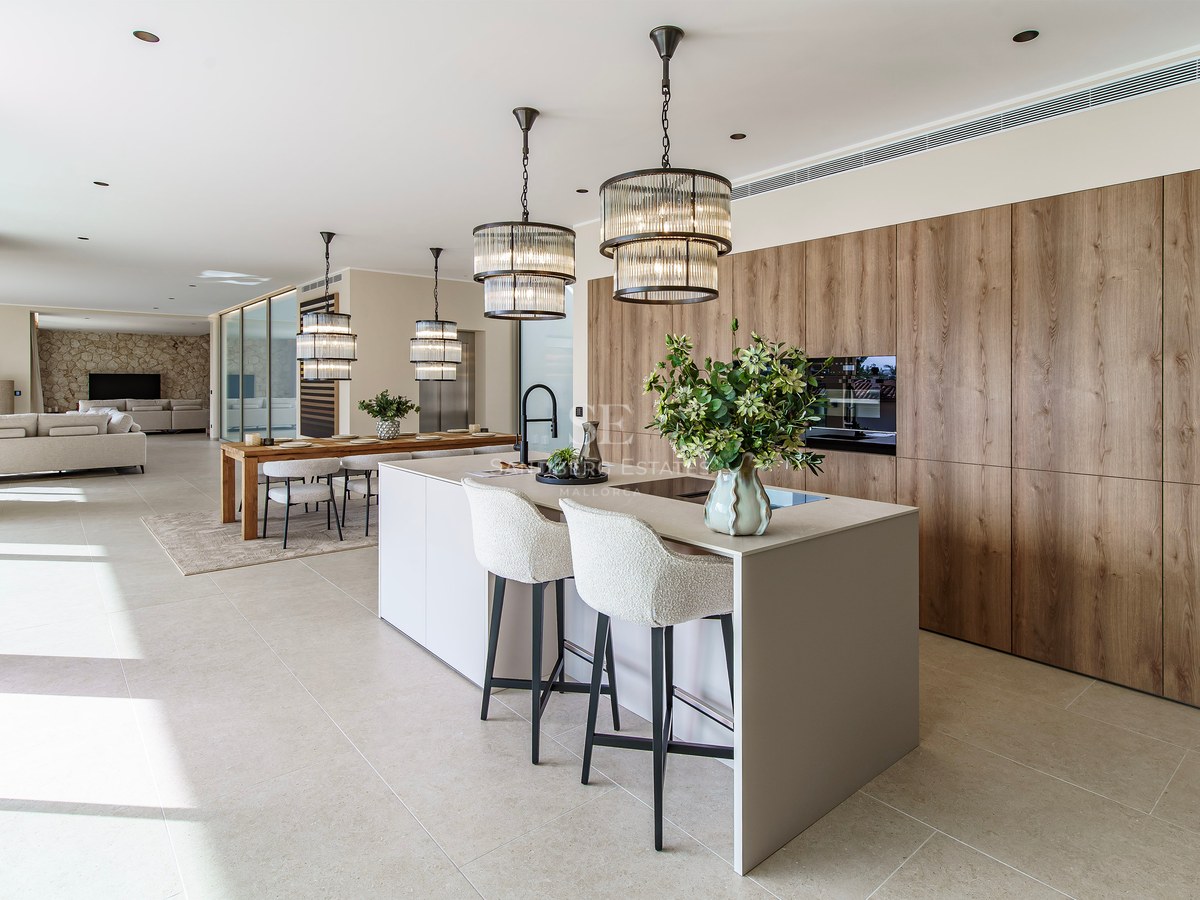 Cuisine moderne avec un grand îlot, tabourets blancs, suspensions design et armoires en bois dans un espace ouvert.