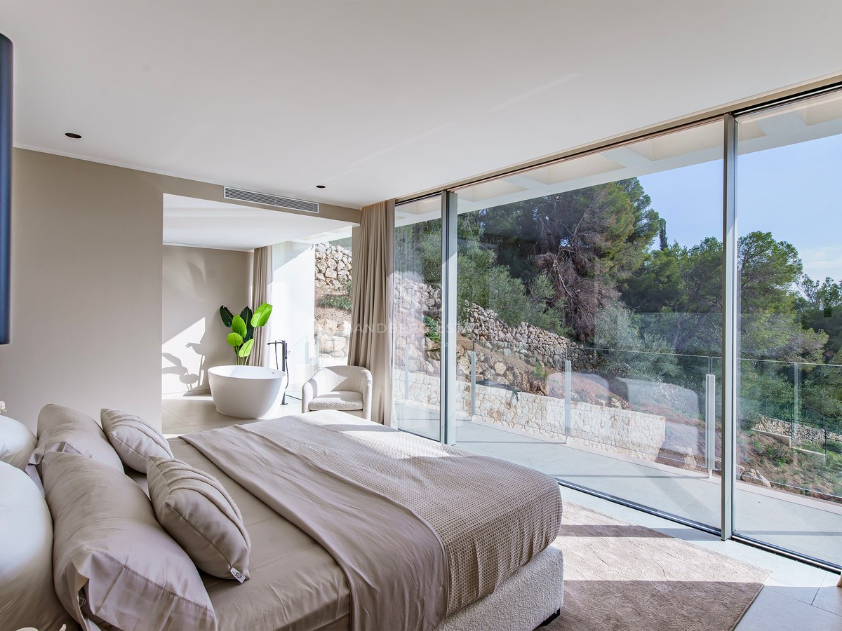 Chambre moderne avec baies vitrées, grand lit aux tons neutres et baignoire îlot avec vue sur le jardin.