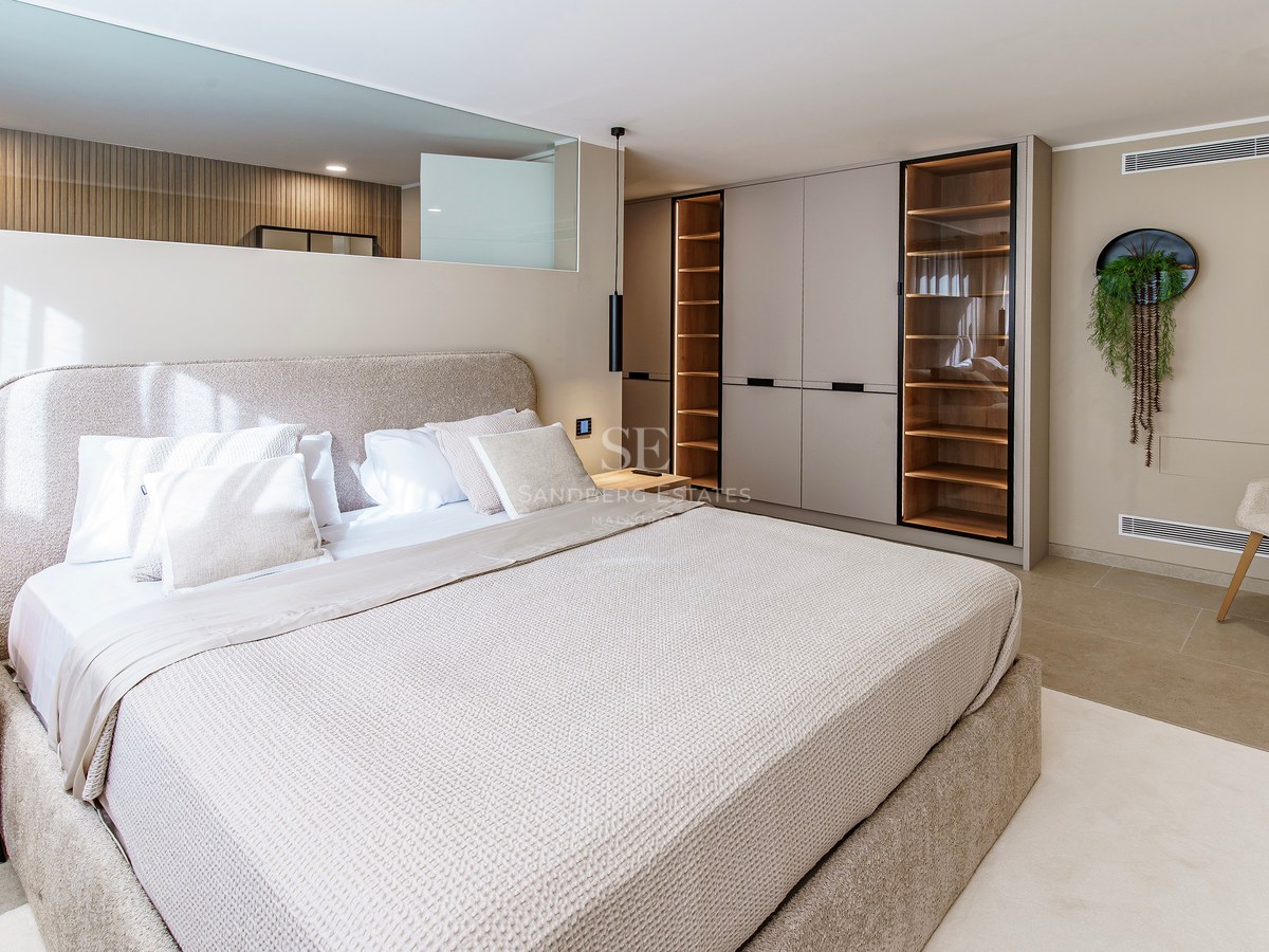 Chambre principale moderne avec grand lit rembourré, armoires encastrées avec éclairage LED et décor neutre.