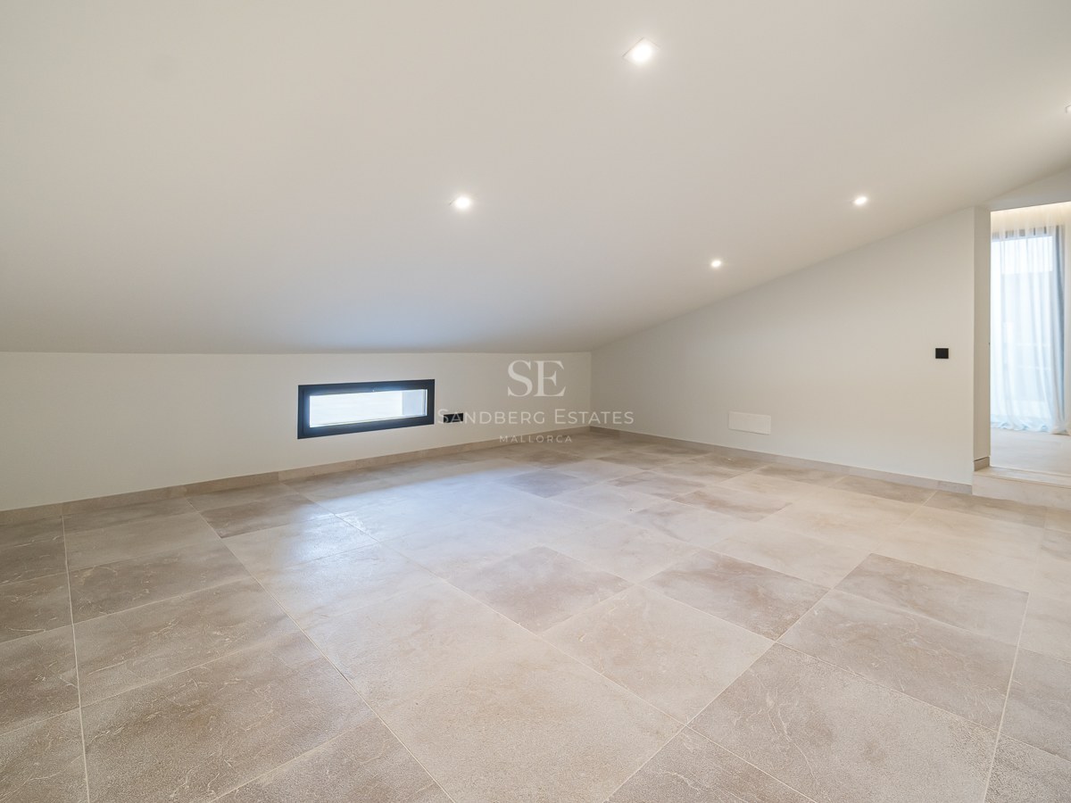 Pièce mansardée vide avec carrelage beige, plafond blanc incliné et spots encastrés.