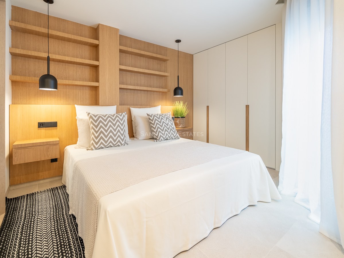Chambre moderne avec mur en chêne clair, étagères intégrées, suspensions noires et grandes armoires blanches.