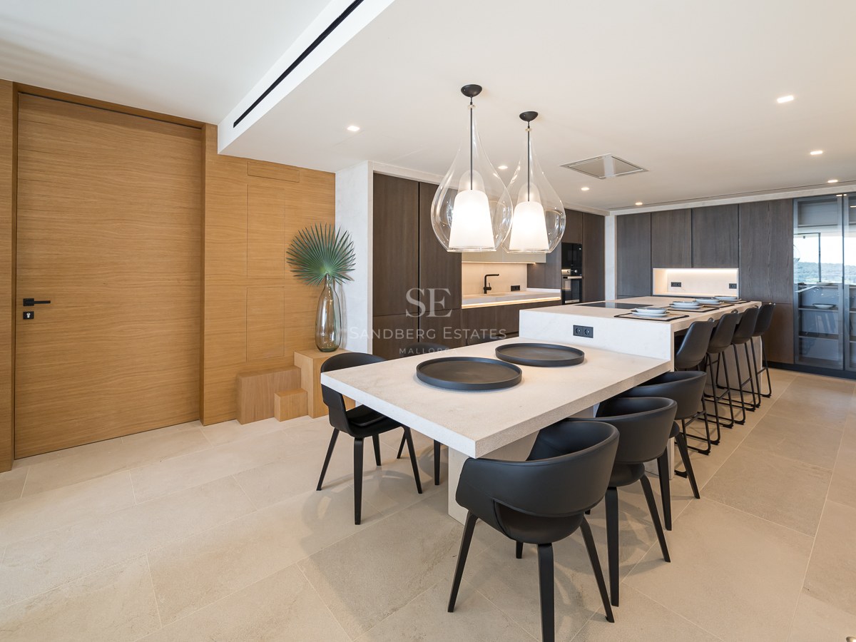 Cuisine moderne avec un grand îlot en pierre, boiseries en chêne, chaises en cuir noir et suspensions en verre.