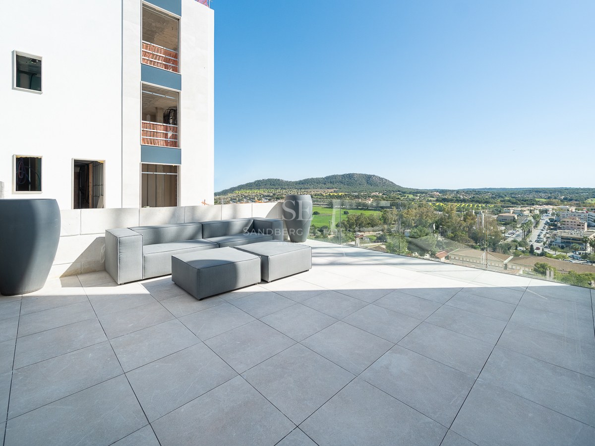 Grande terrasse moderne avec canapés modulables gris, garde-corps en verre et vues dégagées sur la vallée et les montagnes.